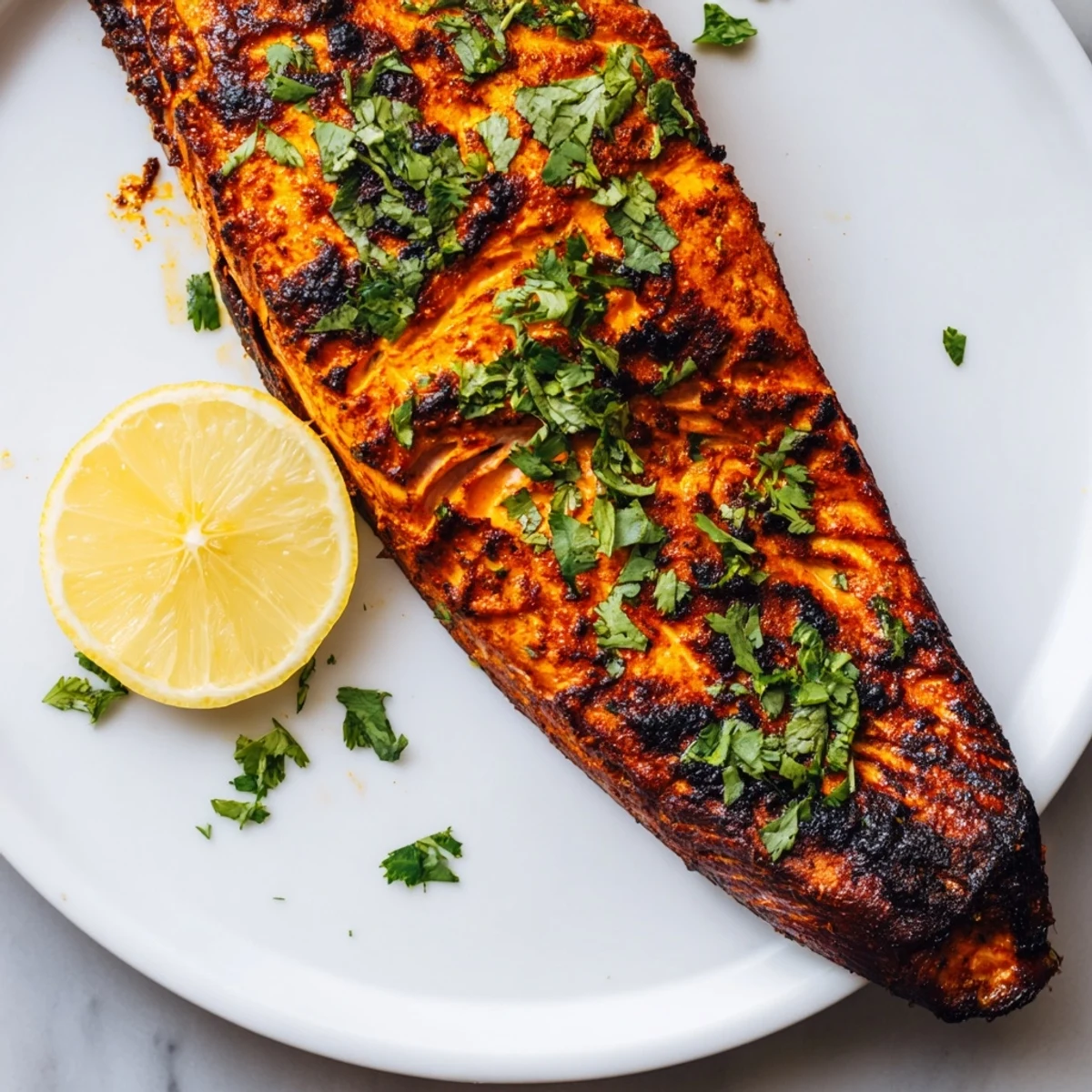 Golden-brown Indian tikka salmon glistens, ready to serve with fresh coriander and lemon wedges.