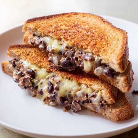 A close-up of a warm, cheesy Black Bean Grilled Cheese sandwich, sliced in half, showing filling.