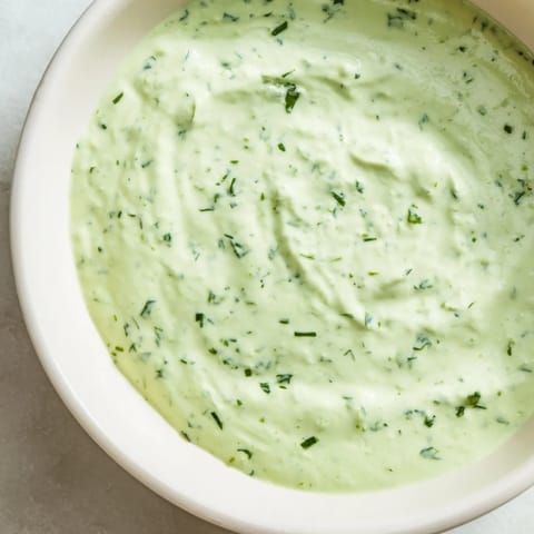 Close-up of creamy Green Goddess Salad Dip in a white bowl, garnished with chopped parsley and chives for a fresh appetizer.  