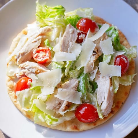 Savory Caesar Chicken Flatbread with sliced chicken, cherry tomatoes, and Parmesan shavings on a wooden board.  