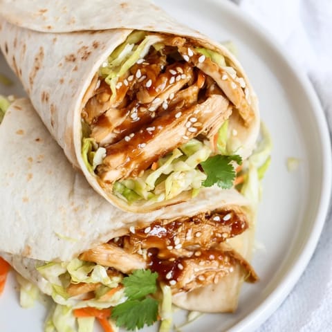 Freshly rolled Teriyaki Chicken Wrap with sesame seeds and cilantro, served on a wooden board with a side of lime wedges.