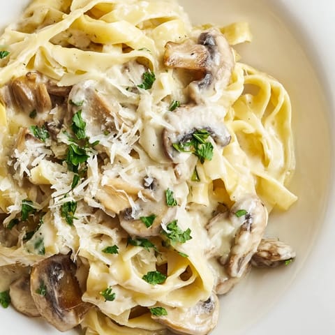 A close-up of Creamy Mushroom Alfredo, featuring al dente pasta draped in luscious garlic cream sauce and savory cremini mushrooms.