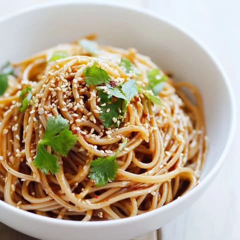 Chilled noodles coated in spicy sesame dressing, garnished with crisp cucumber slices and fresh cilantro for a refreshing salad.  