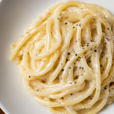 A close-up of Spaghetti Cacio e Pepe, highlighting the silky, cheese-coated noodles and fragrant pepper specks.