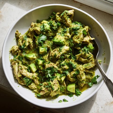 A close-up of tender Chicken Chili Verde in a rustic bowl, garnished with creamy avocado slices and fresh radishes.