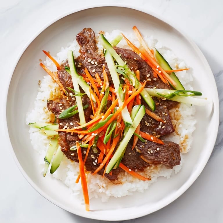A steaming bowl of bulgogi beef, served over fluffy rice and garnished with fresh scallions and seeds.
