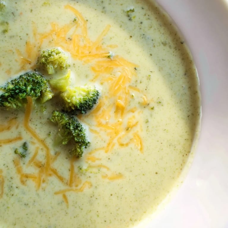 Close-up of rich broccoli cheddar soup topped with extra grated cheese, served beside crusty artisan bread.