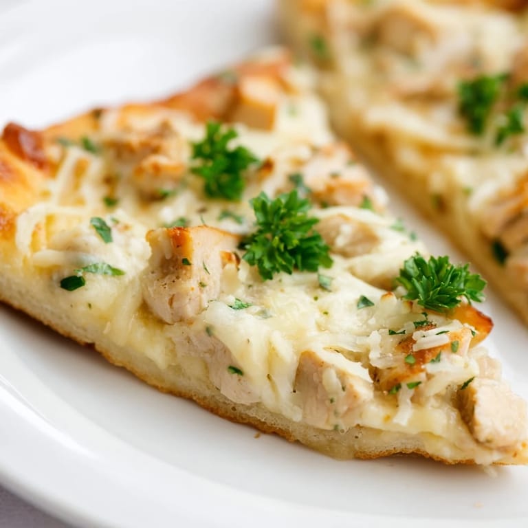 Golden, cheesy Chicken Alfredo Pizza with tender chicken and creamy sauce on a rustic wooden table.  