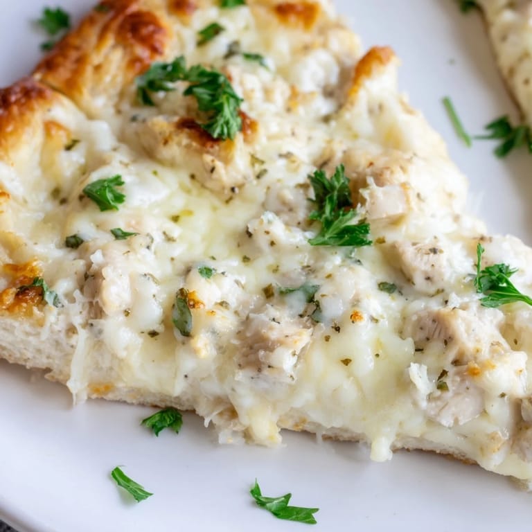 Freshly baked Chicken Alfredo Pizza with golden crust, melted cheese, and parsley garnish on a marble surface.