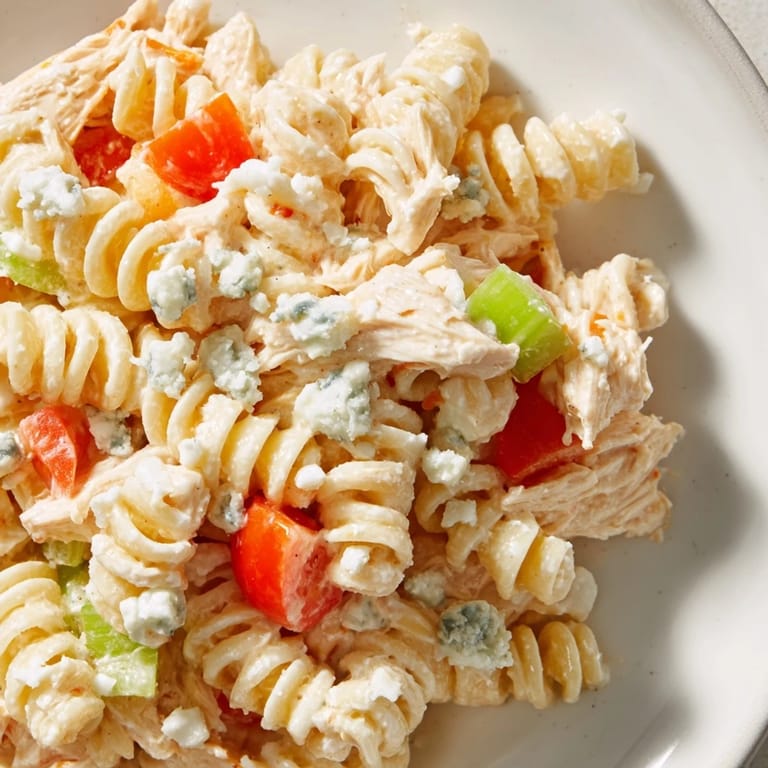Serving suggestion for Buffalo Chicken Pasta Salad garnished with crumbled blue cheese and fresh chives on a picnic table.  