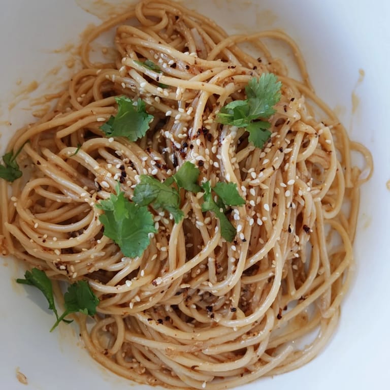 Spicy Sesame Noodle Salad served in a white bowl, garnished with green onions and a vibrant chili oil drizzle.