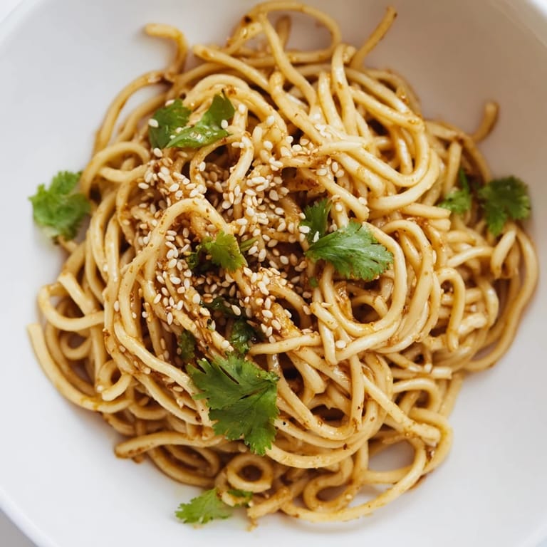 A close-up of Spicy Sesame Noodle Salad with toasted sesame seeds and chopped peanuts over a colorful vegetable medley.  
