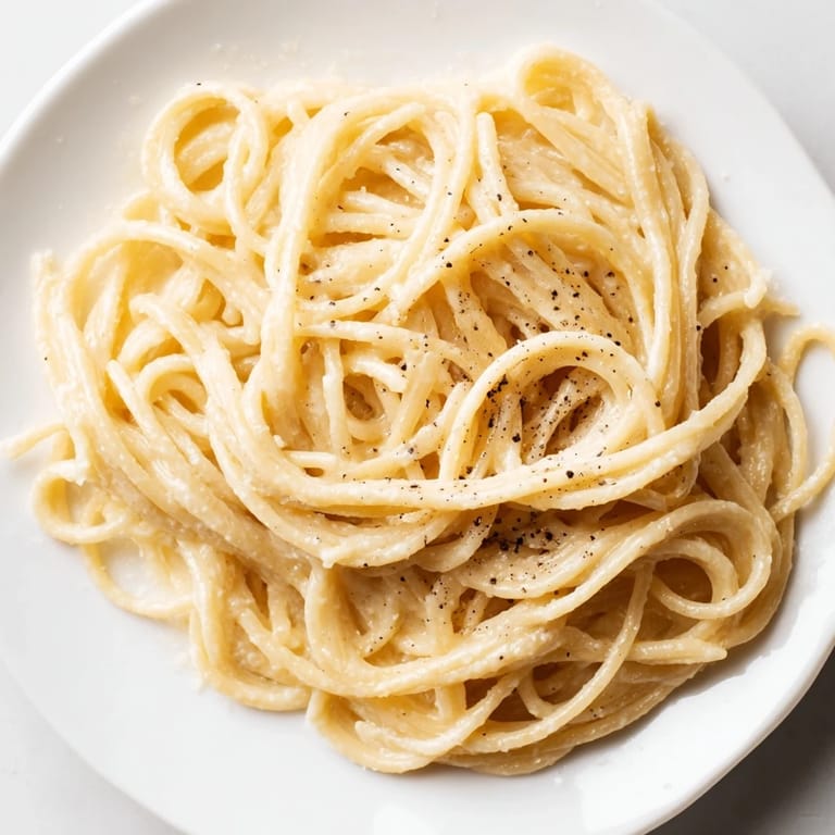 Steaming plate of Spaghetti Cacio e Pepe, garnished with grated Pecorino Romano and black pepper.