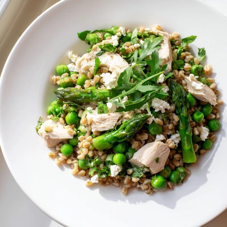 Vibrant bowl of Warm Spring Farro Chicken Salad with juicy chicken, blanched spring peas, and a zesty lemon herb dressing garnish.