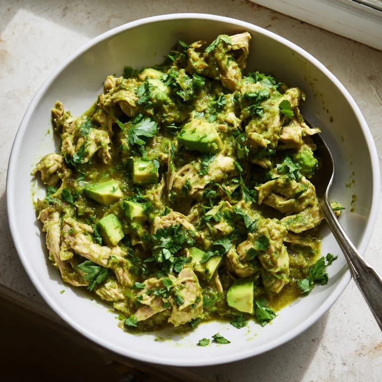 A close-up of tender Chicken Chili Verde in a rustic bowl, garnished with creamy avocado slices and fresh radishes.